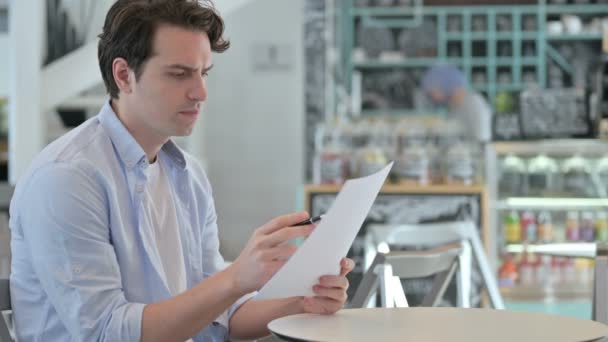 Молодой человек читает документы в кафе — стоковое видео