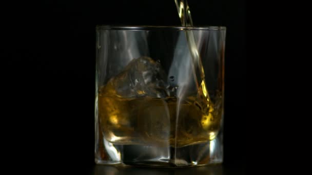 Langzame beweging van het gieten van Whiskey in glas met ijs in donkere achtergrond — Stockvideo