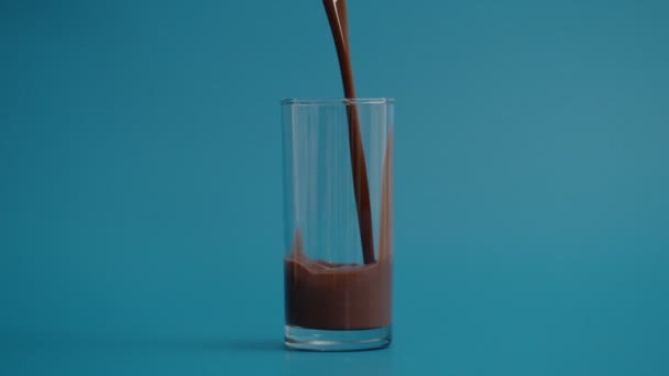 Mouvement super lent de verser du lait au chocolat dans du verre transparent, fond bleu — Video