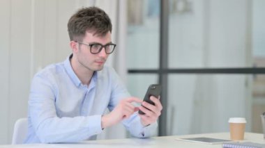 Ofiste akıllı telefon kullanan çekici genç adam. 