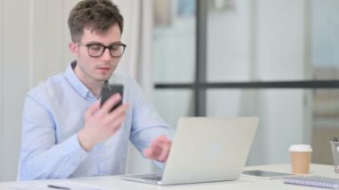 Dizüstü bilgisayarlı genç adam telefonda konuşuyor. 