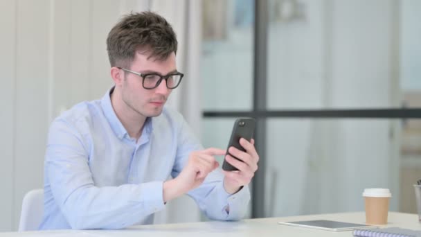 Młody człowiek reaguje na stratę na smartfonie w biurze — Wideo stockowe