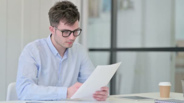 Молодий чоловік читає документи в офісі — стокове відео