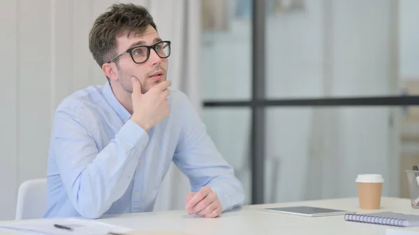 Jeune homme assis dans le bureau pensant — Photo