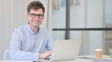 Dizüstü bilgisayarlı genç adam Kameraya gülümsüyor 