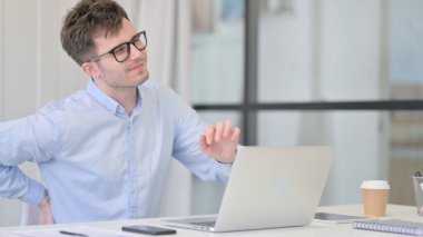 Dizüstü bilgisayarı olan genç adam sırt ağrısı çekiyor. 