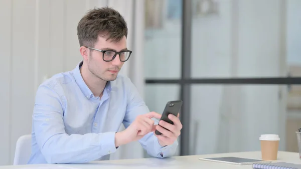 Jeune homme attrayant utilisant Smartphone au bureau — Photo