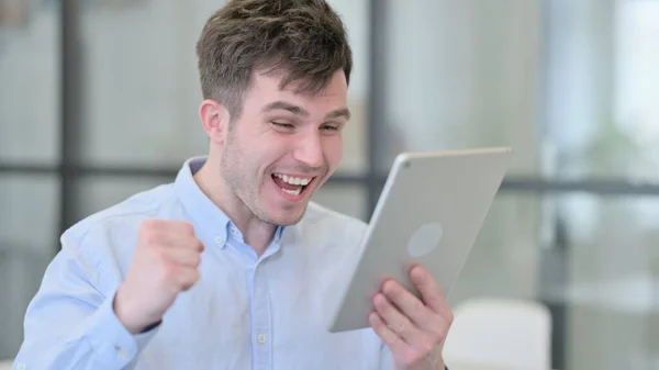 Молодой человек празднует успех на планшете — стоковое фото