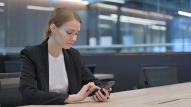 İş yerinde akıllı telefon kullanan çekici bir iş kadını. 