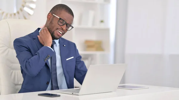 Hombre de negocios africano cansado con el ordenador portátil que tiene dolor de cuello en la oficina —  Fotos de Stock