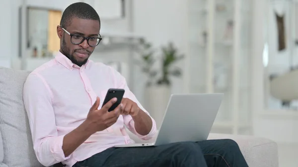 Hombre africano usando Smartphone y Laptop en casa —  Fotos de Stock