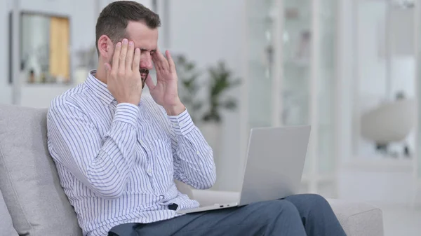 Gestresster junger Mann mit Laptop hat zu Hause Kopfschmerzen — Stockfoto