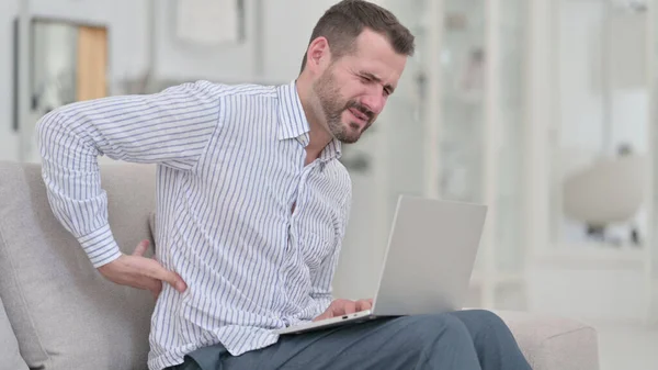 Jeune homme avec douleur au dos en utilisant un ordinateur portable à la maison — Photo