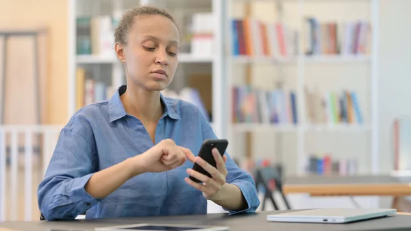 Schwere Afrikanerin benutzt Smartphone in Bibliothek — Stockfoto