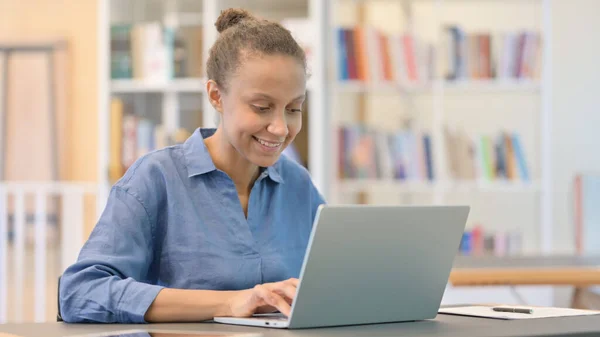 Glada afrikanska kvinna som arbetar på laptop i biblioteket — Stockfoto