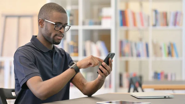 Atractivo joven africano usando Smartphone en la biblioteca —  Fotos de Stock