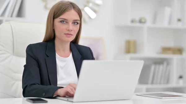 Молодая предпринимательница с ноутбуком смотрит в камеру в офисе — стоковое фото