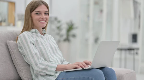 Ung kvinna med bärbar dator ler mot kameran hemma — Stockfoto