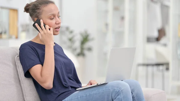 Afrikansk kvinna med bärbar dator prata på telefon hemma — Stockfoto