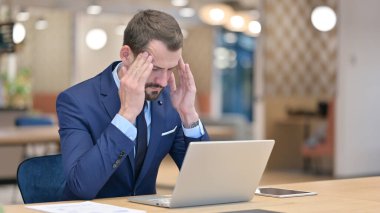 Dizüstü bilgisayarı olan orta yaşlı iş adamı ofiste baş ağrısı çekiyor 