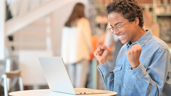 Spännande afrikansk kvinna firar framgång på laptop på Cafe — Stockfoto