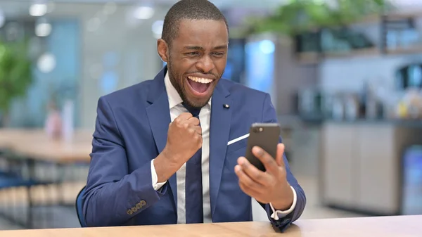 非洲商人在办公室用智能手机庆祝成功 — 图库照片