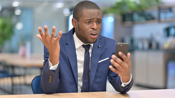 Empresario africano reacciona al fracaso en el teléfono inteligente en la oficina —  Fotos de Stock