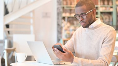 Kafede akıllı telefon ve dizüstü bilgisayar kullanan Afrikalı adam.