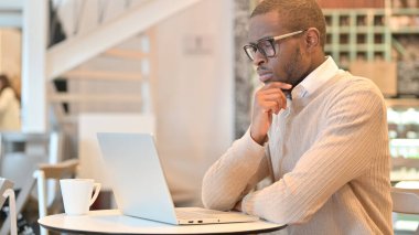 Cafe 'de laptopta düşünen ve çalışan dalgın bir Afrikalı.
