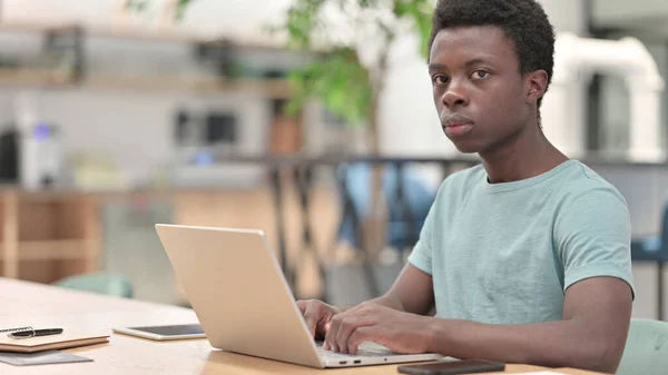 Allvarlig ung afrikansk man med bärbar dator tittar på kameran — Stockfoto