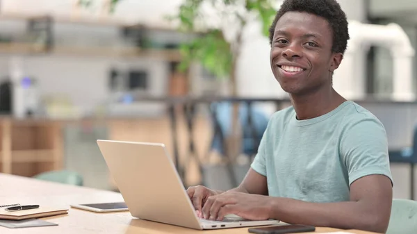 Ung afrikansk man med bärbar dator ler mot kameran — Stockfoto