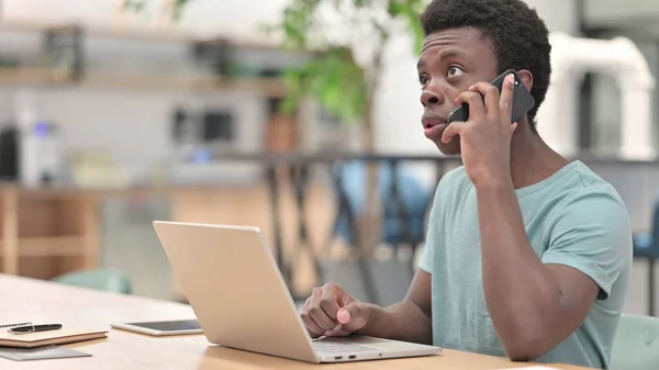Ung afrikansk man som använder smartphone och laptop — Stockfoto