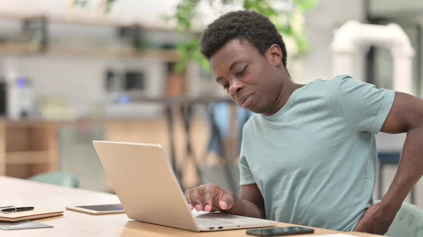 Ung afrikansk man med bärbar dator har ryggvärk — Stockfoto