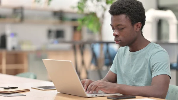 Ung afrikansk man som arbetar med bärbar dator, skriva — Stockfoto