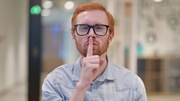 Serio joven pelirrojo poniendo dedo en los labios —  Fotos de Stock