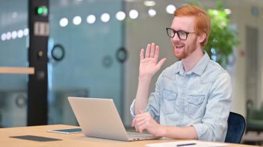 Ofisteki dizüstü bilgisayardan konuşan neşeli kızıl saçlı adam. 