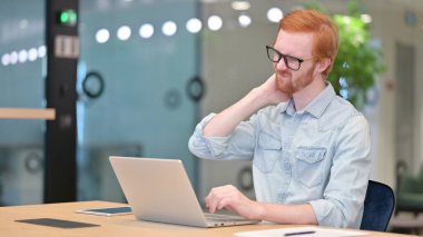 Dizüstü bilgisayarlı yorgun kızıl saçlı adamın ofisinde boyun ağrısı var. 