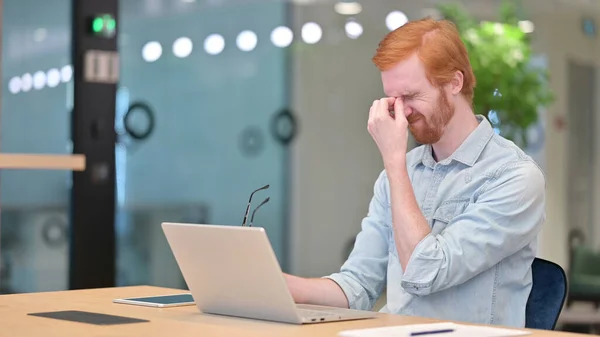 Stressé jeune rousse homme avec ordinateur portable ayant mal à la tête au bureau — Photo