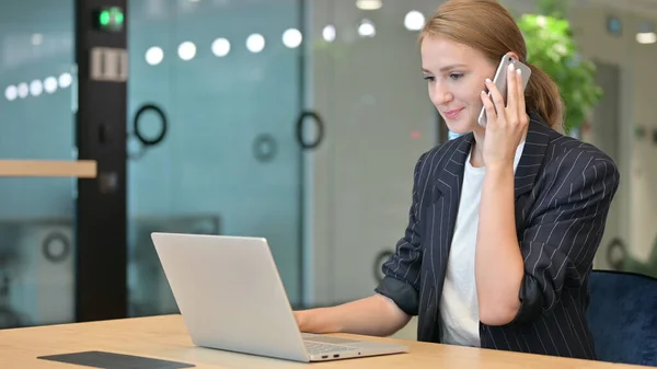 Молодая предпринимательница с ноутбуком разговаривает по телефону, переговоры — стоковое фото