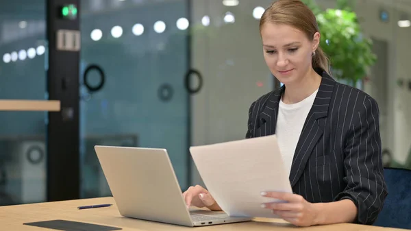 Серьёзная молодая предпринимательница с документами для чтения ноутбуков в офисе — стоковое фото