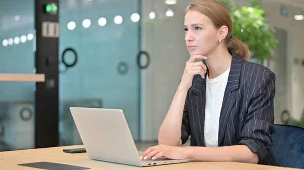Привлекательная молодая предпринимательница думает и работает над ноутбуком в офисе — стоковое фото