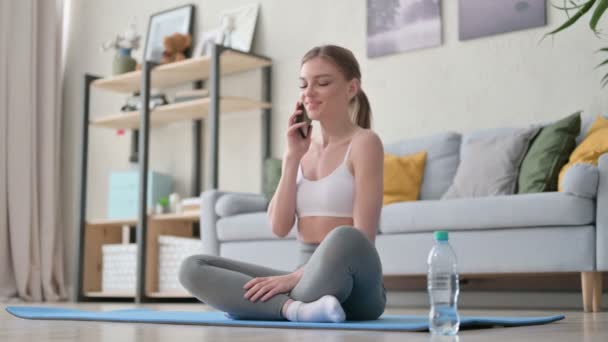 Mujer joven hablando en Smartphone en Yoga Mat en casa — Vídeo de stock