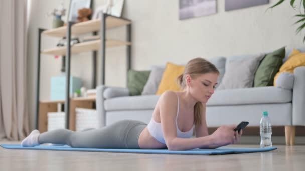 Mujer joven usando Smartphone acostado en estera de yoga — Vídeo de stock