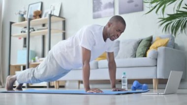 Evde yoga yaparken yorgun Afrikalı adam şınav çekiyor.