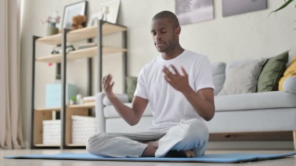 Ung afrikansk man mediterar på yogamattan hemma — Stockvideo