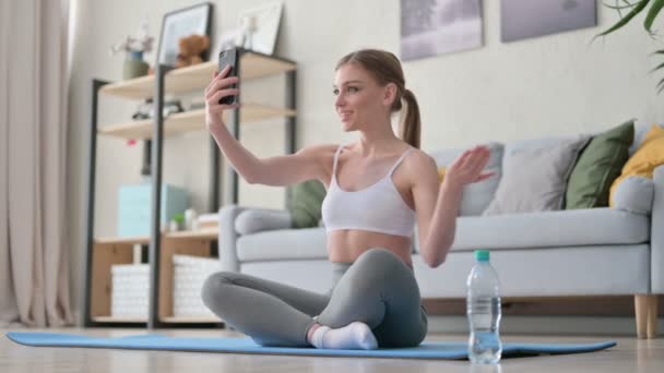 Mujer joven hablando en videollamada en Smartphone mientras está sentada en Yoga Mat — Vídeo de stock