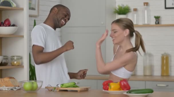 Sportig kvinna och afrikansk man dansar i köket — Stockvideo