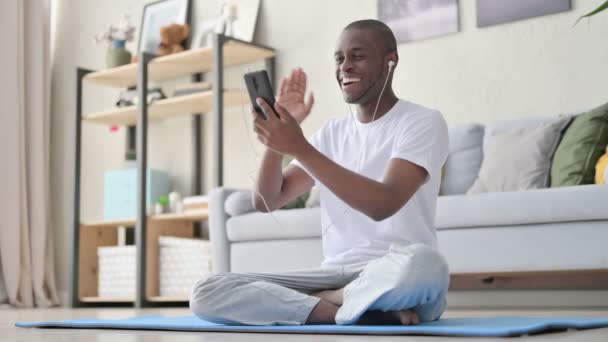 Hombre africano hablando en videollamada mientras está sentado en la esterilla de yoga — Vídeos de Stock