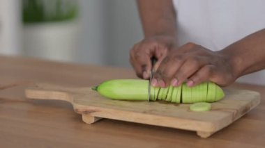 Kesme tahtasında salatalık kesen Afrikalı adamın ellerini yakın plan çek.