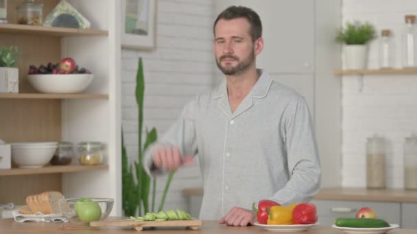 Молодой человек показывает пальчики вниз, стоя на кухне — стоковое видео